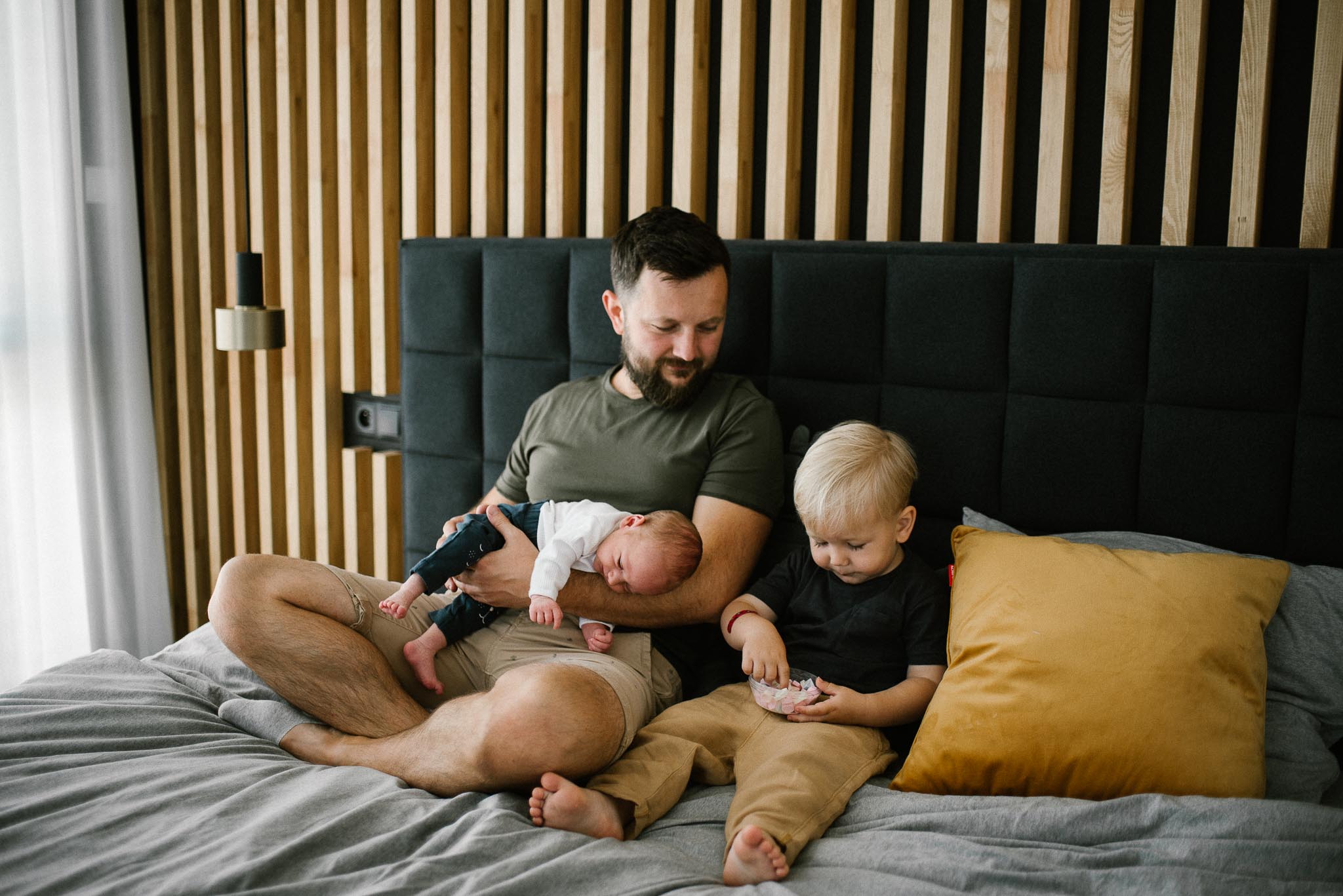 Tata z synami siedzi na łóżku - sesja noworodkowa lifestyle w Poznaniu