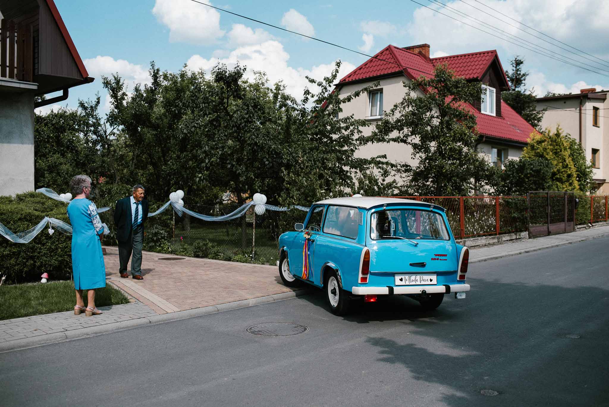 Państwo młodzi wsiadają do starego, niebieskiego trabanta - ślub w stodole Dyrkowo