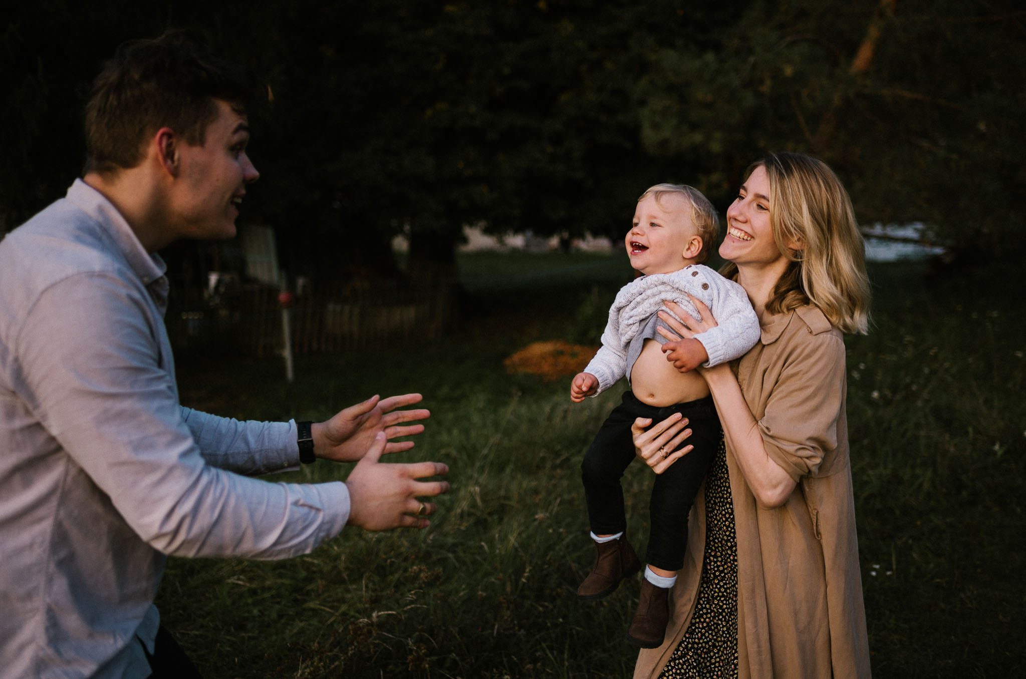 Mama trzyma synka na rękach i podaje tacie - sesja w plenerze jesienią w Poznaniu