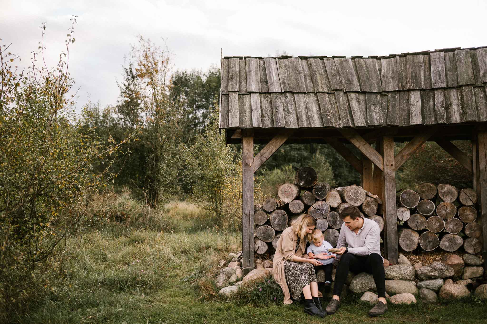 Mama i tata siedzą przy belkach drewnianych i się przytulają - jesienna sesja rodzinna w plenerze Poznań