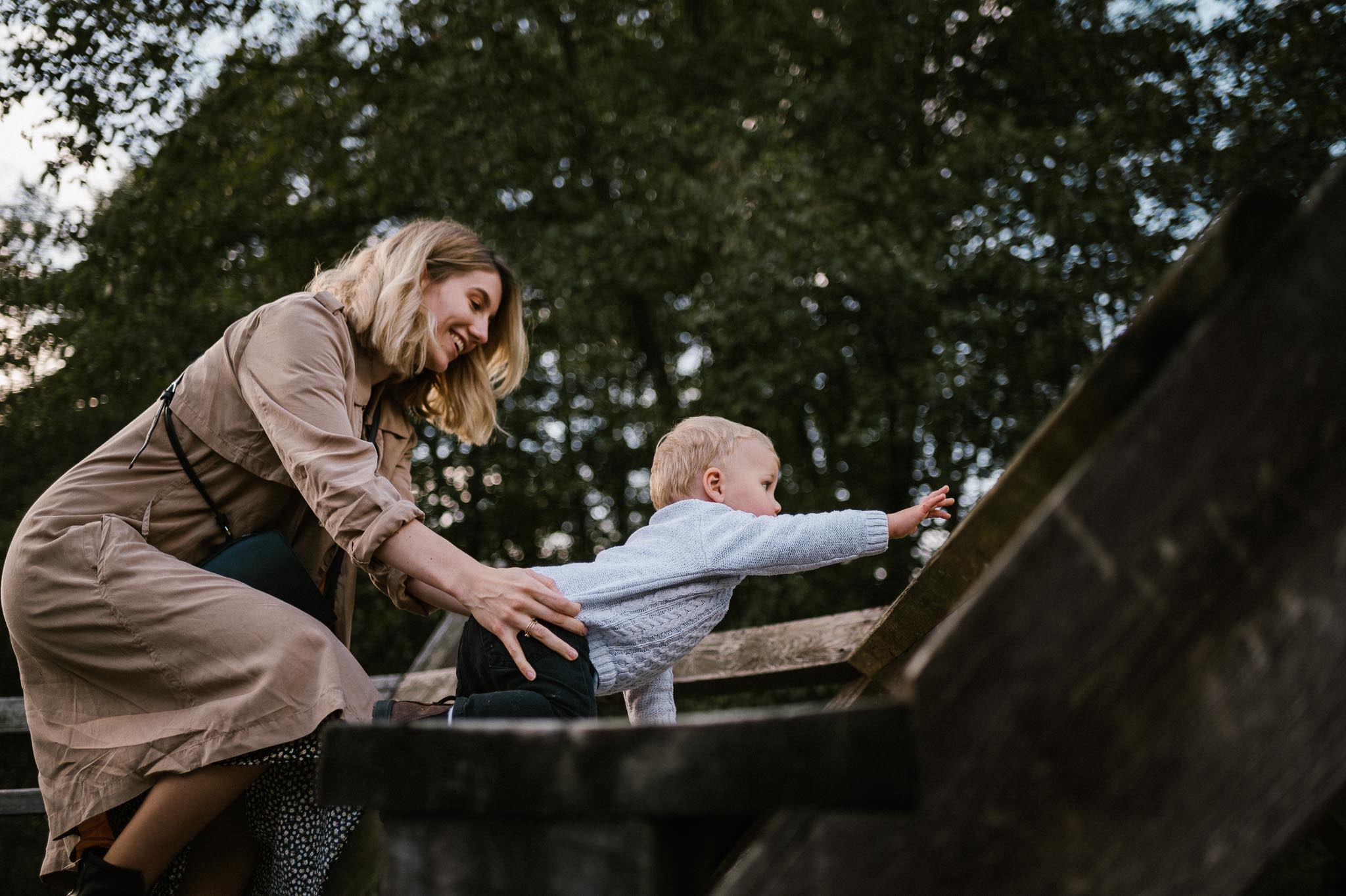 Mama trzyma synka, który wspina się na drewnianą konstrukcję  sesja rodzinna w plenerze jesienna Poznań