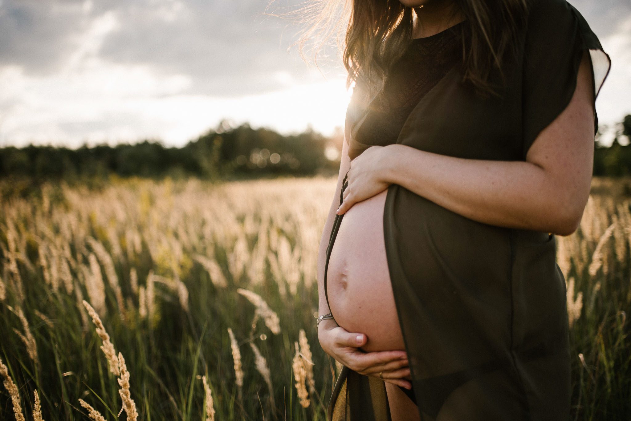 Kobieta z odsłoniętym brzuchem na łące -Sesja ciążowa na polu w plenerze Poznań