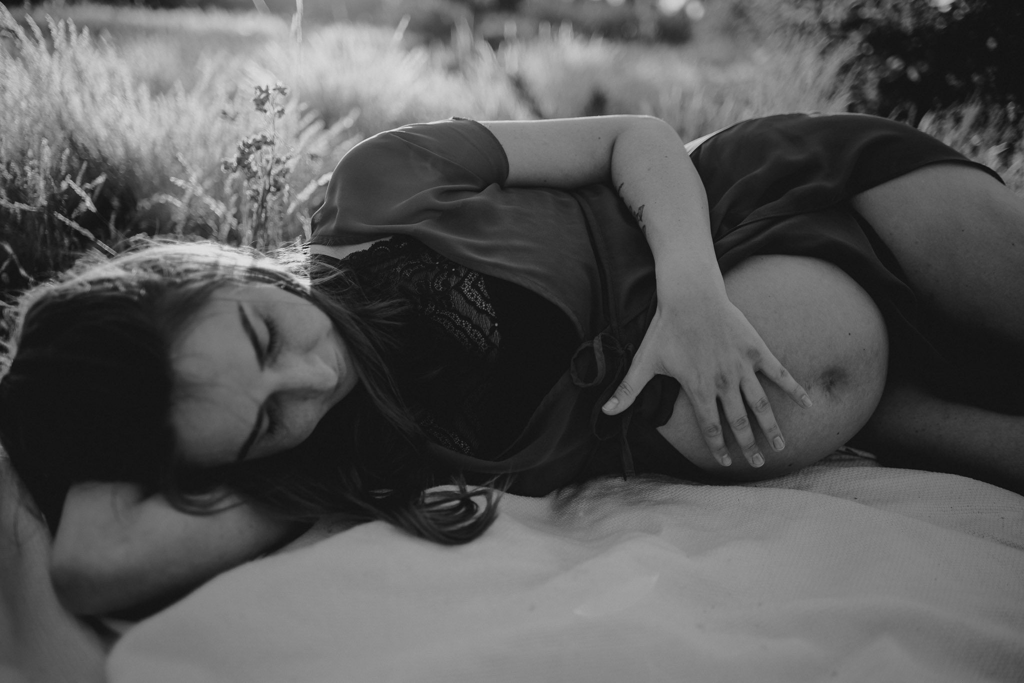 Kobieta z odsłoniętym brzuchem ciążowym na łące na kocu-Sesja ciążowa na polu w plenerze Poznań
