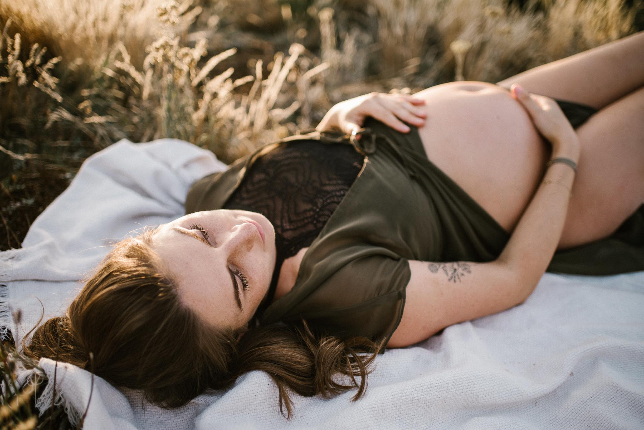 Kobieta z odsłoniętym brzuchem ciążowym na łące na kocu-Sesja ciążowa na polu w plenerze Poznań