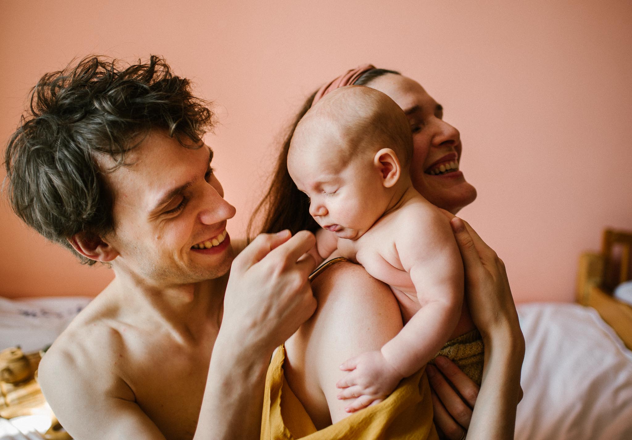 Mama i tata uśmiechają się do niemowlęcia, mama trzyma bobasa - Sesja niemowlęca lifestyle w domu Poznań