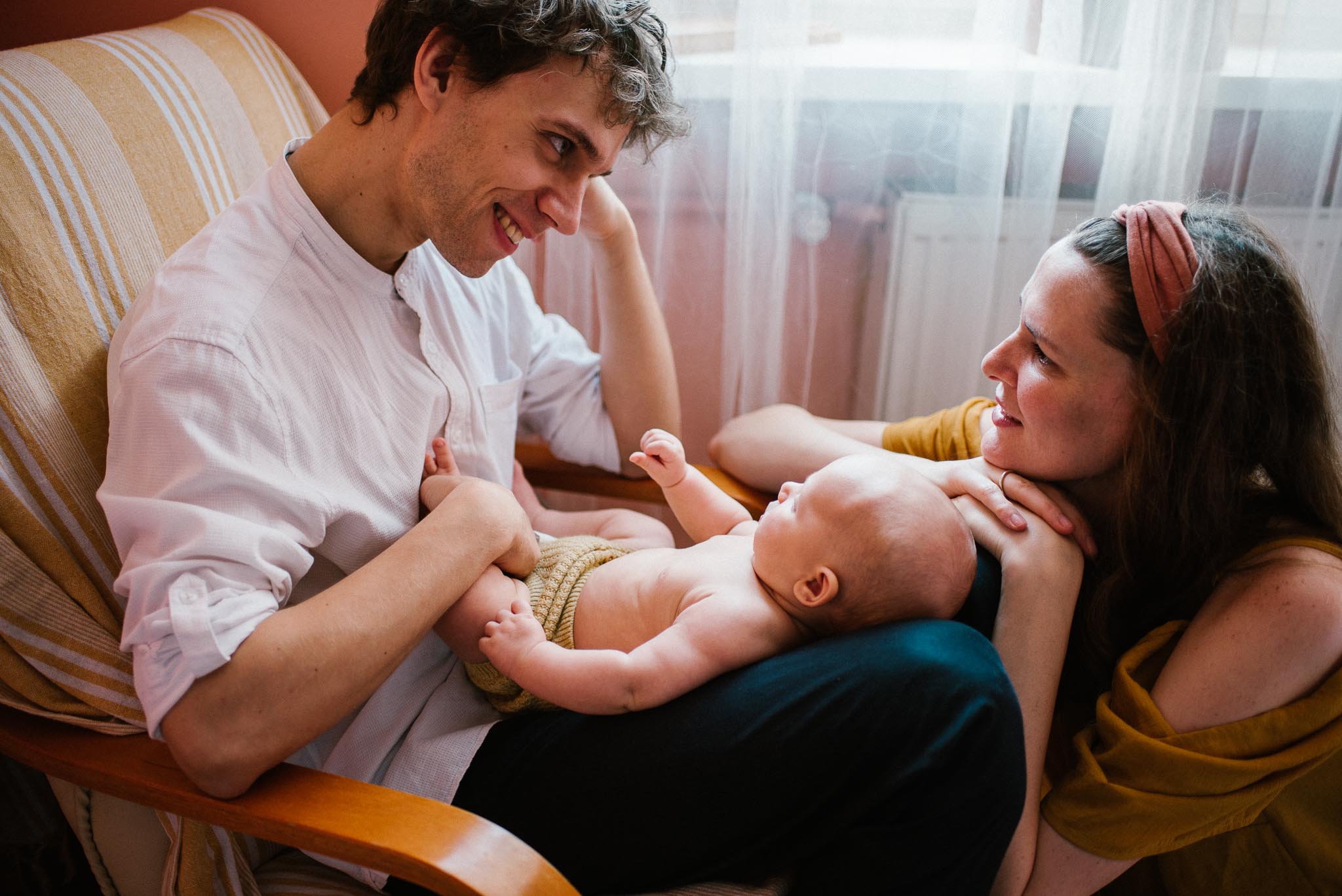 Tata trzyma niemowlę na kolanach, mama siedzi obok nich -Sesja niemowlęca lifestyle w domu Poznań