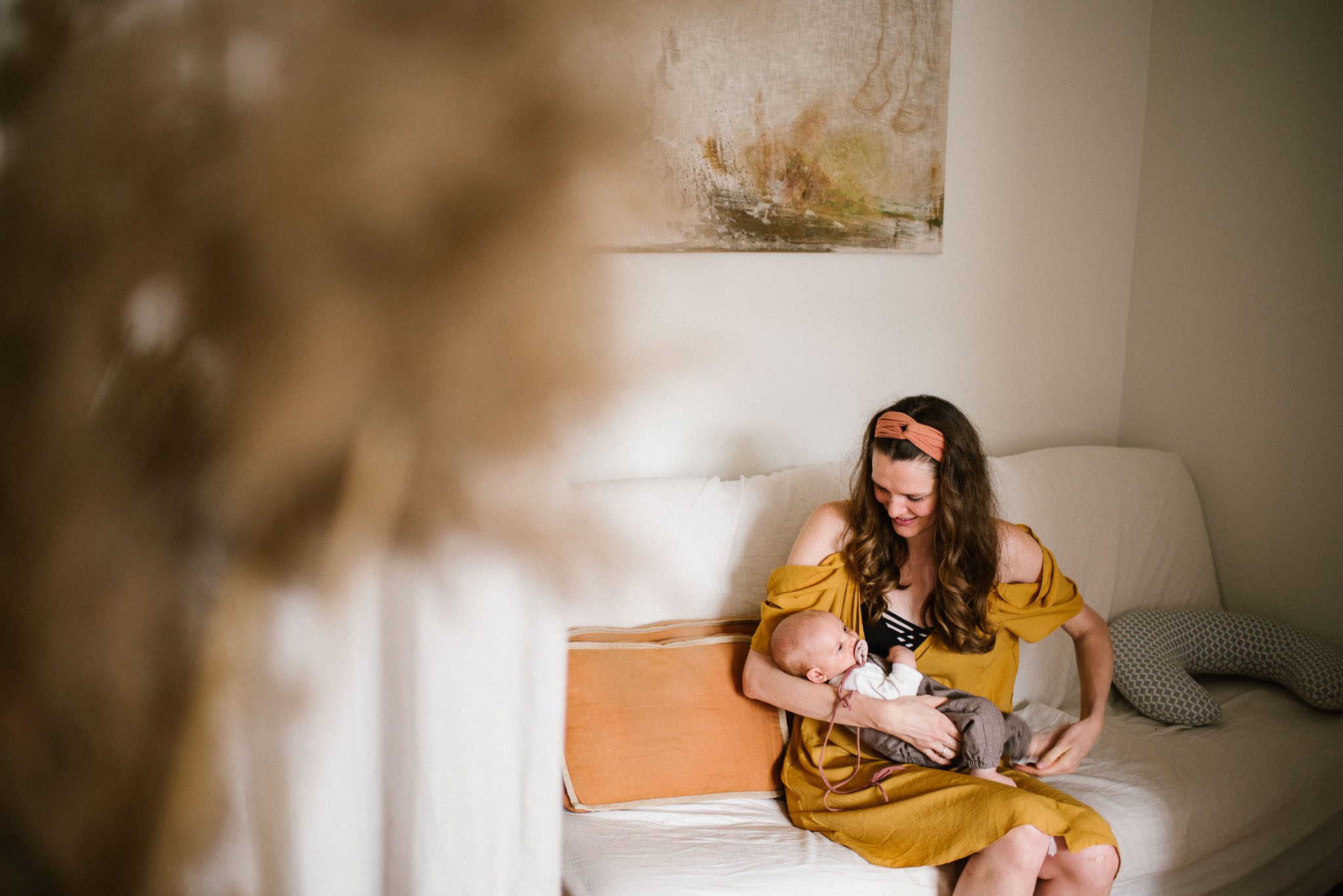 Mama siedzi z niemowlęciem na sofie - Sesja niemowlęca lifestyle w domu Poznań