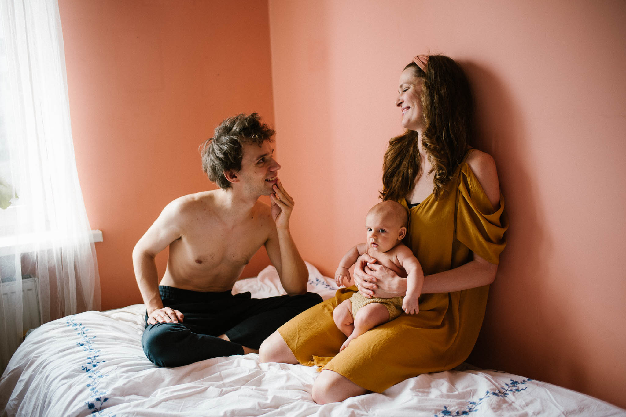 Mąż i żona z niemowlęciem siedzą razem na łóżku - sesja niemowlęca lifestyle w domu Poznań