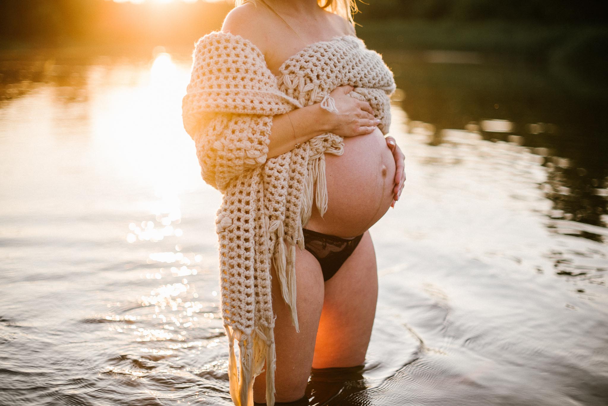 Kobieta obejmuje nagi brzuch ciążowy - Sesja ciążowa w plenerze w wodzie Poznań