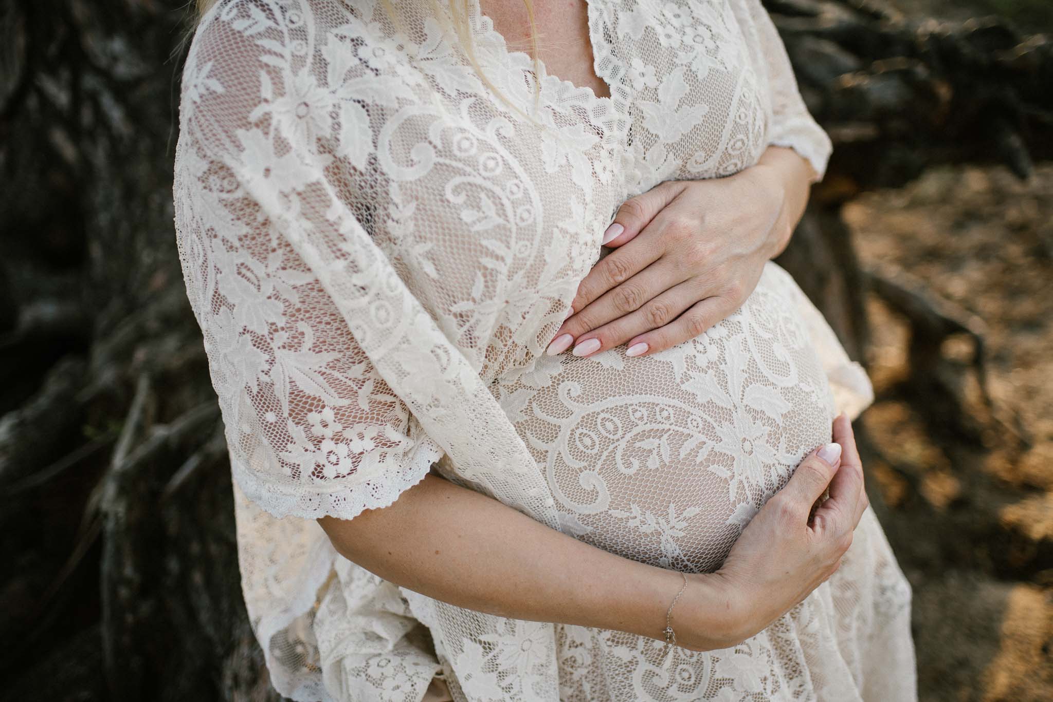 Kobieta obejmuje ciążowy brzuch w koronkowej sukni w stylu boho - Sesja ciążowa w plenerze w wodzie Poznań