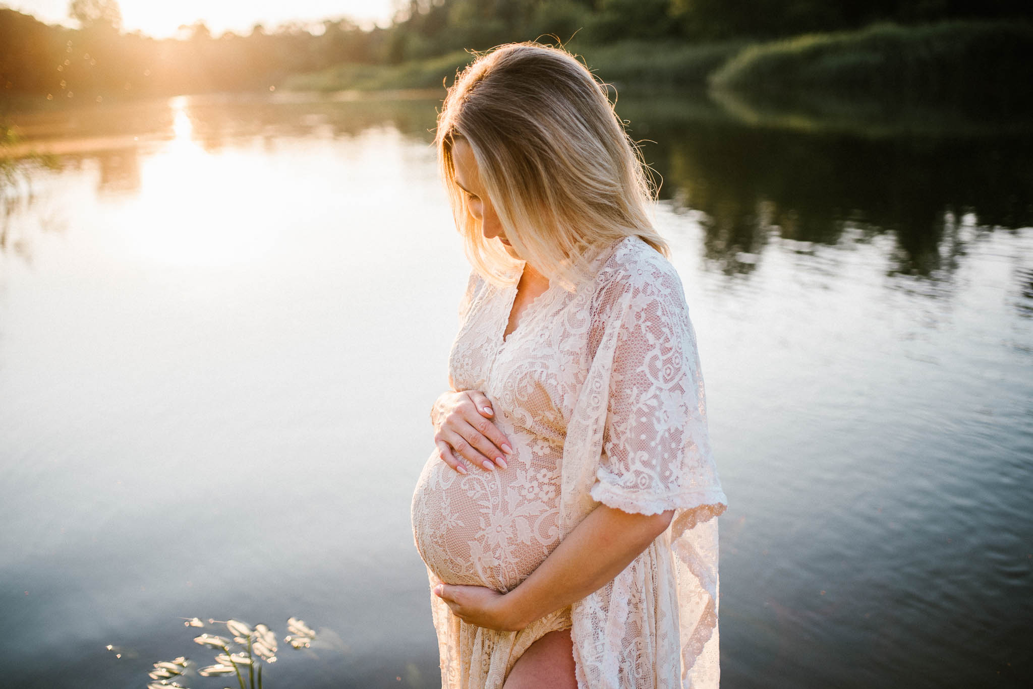 Kobieta w ciąży w koronkowej długiej sukni na tle jeziora - Sesja ciążowa w plenerze w wodzie Poznań