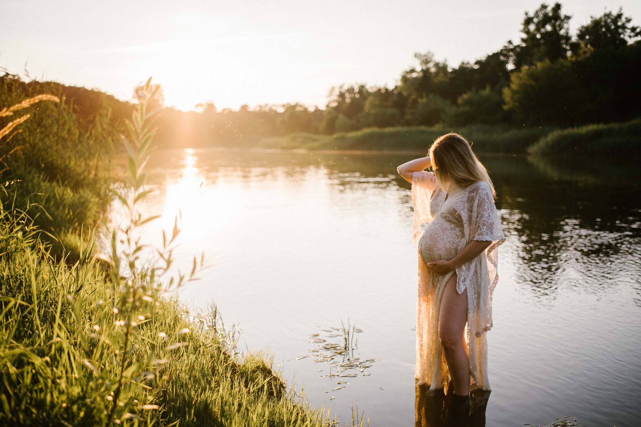 Kobieta wchodzi do jeziora i obejmuje ciążowy brzuch - Sesja ciążowa w plenerze w wodzie Poznań